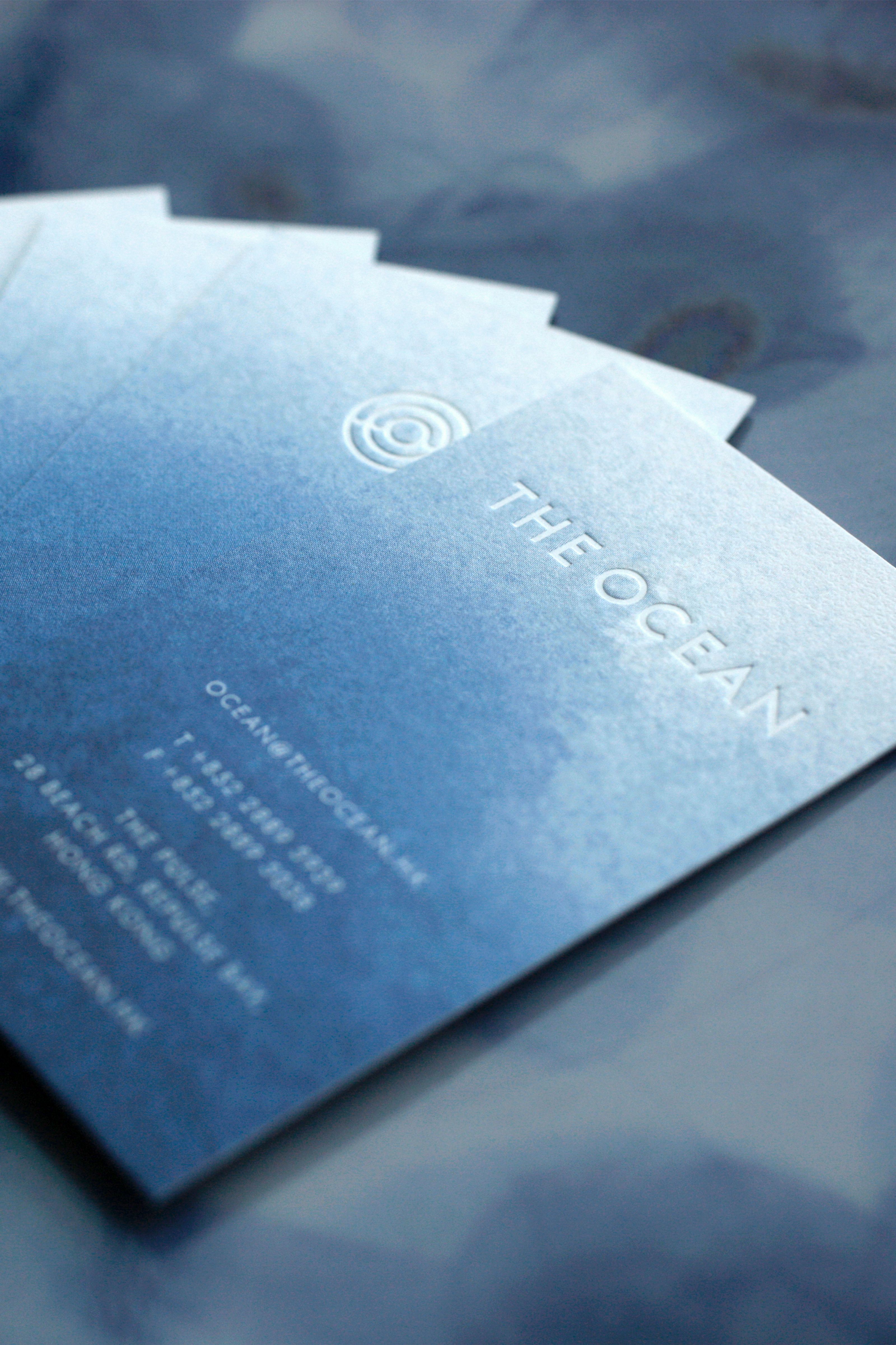 A fanned stack of blue gradient business cards for 'THE OCEAN' with embossed text and contact details.