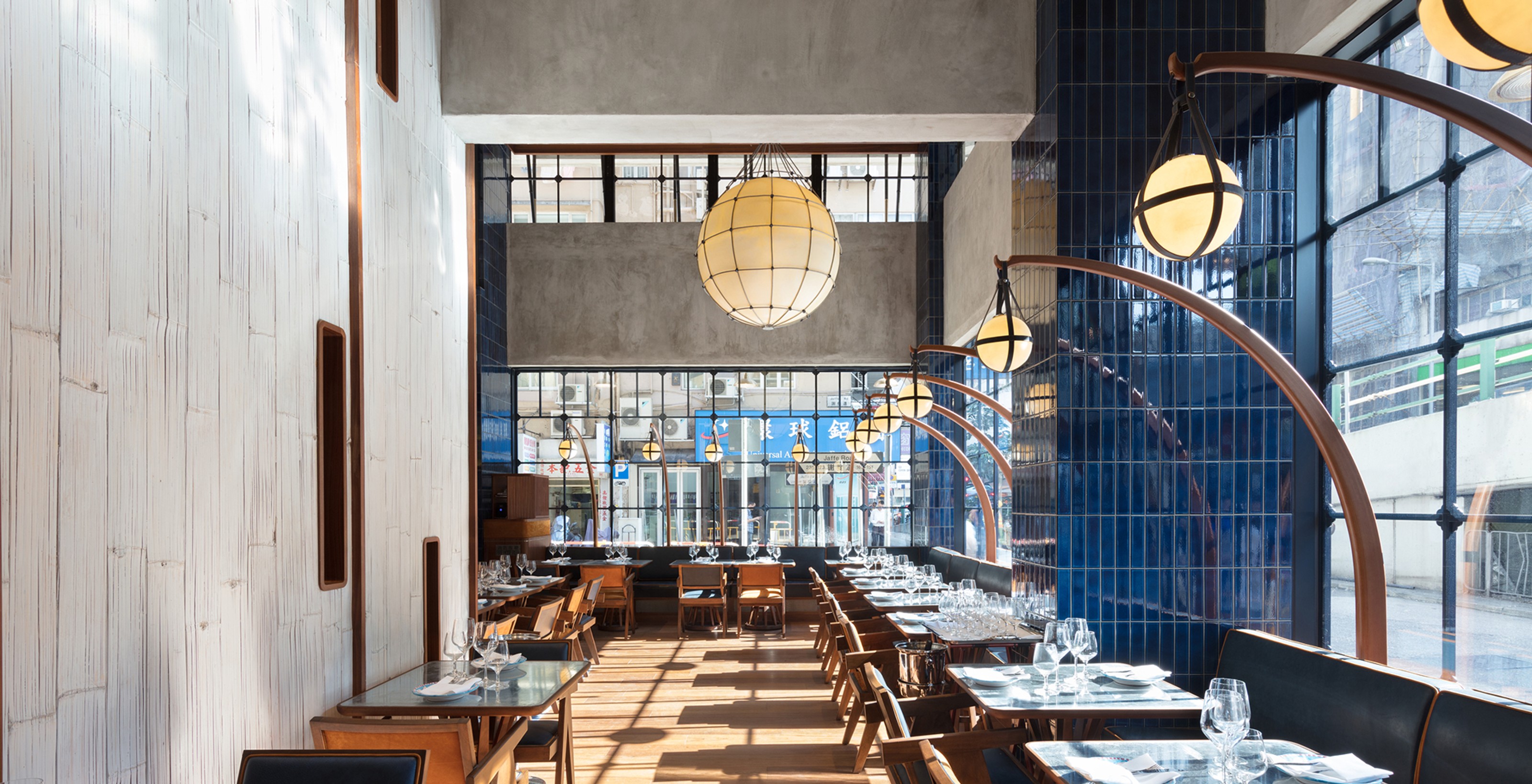 Modern restaurant interior with a long dining area, textured white wall, blue tiled wall, and globe lights on curved arches.