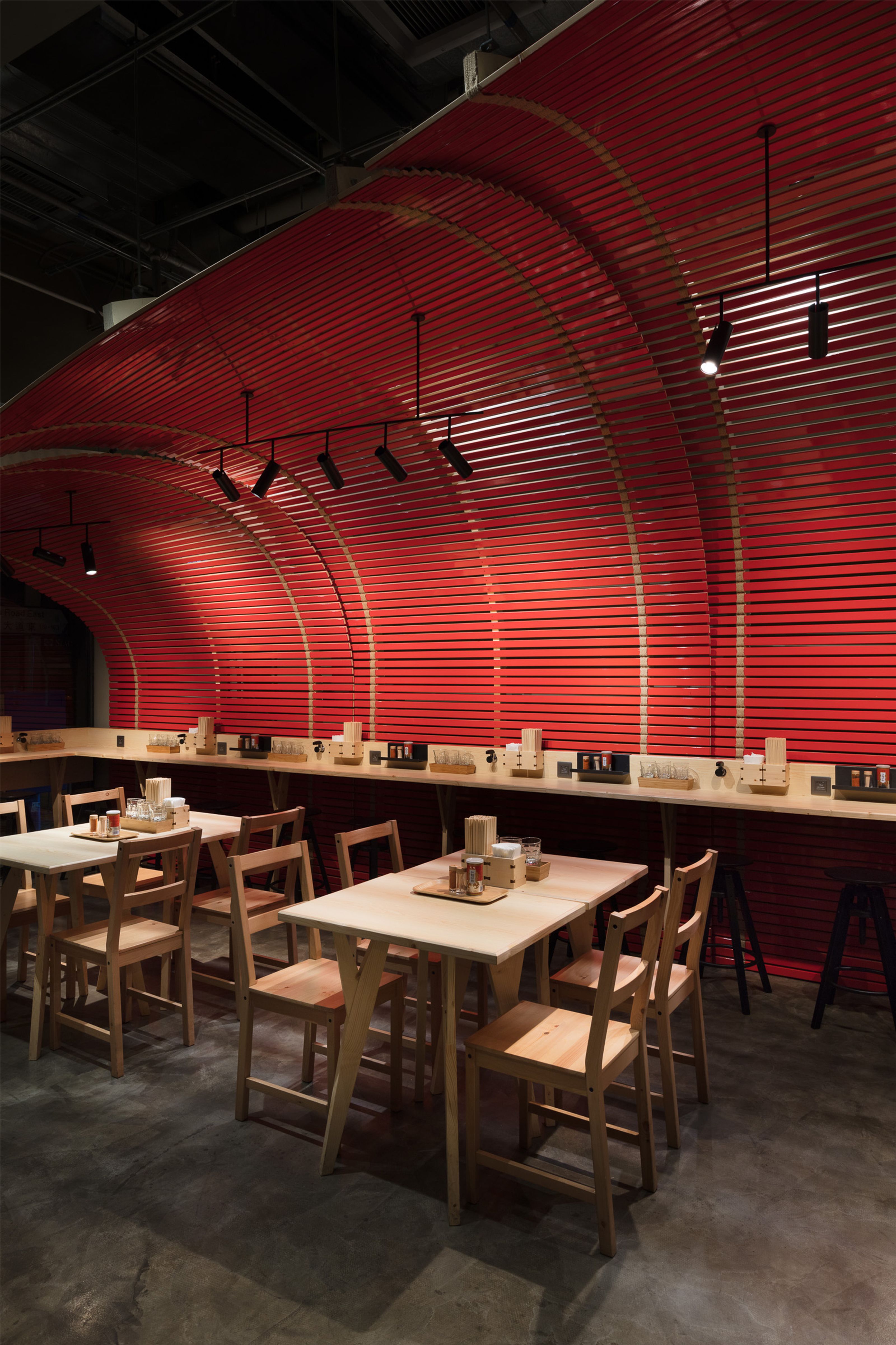 Modern restaurant interior with a curved red slatted wall and ceiling, light wood tables and chairs.