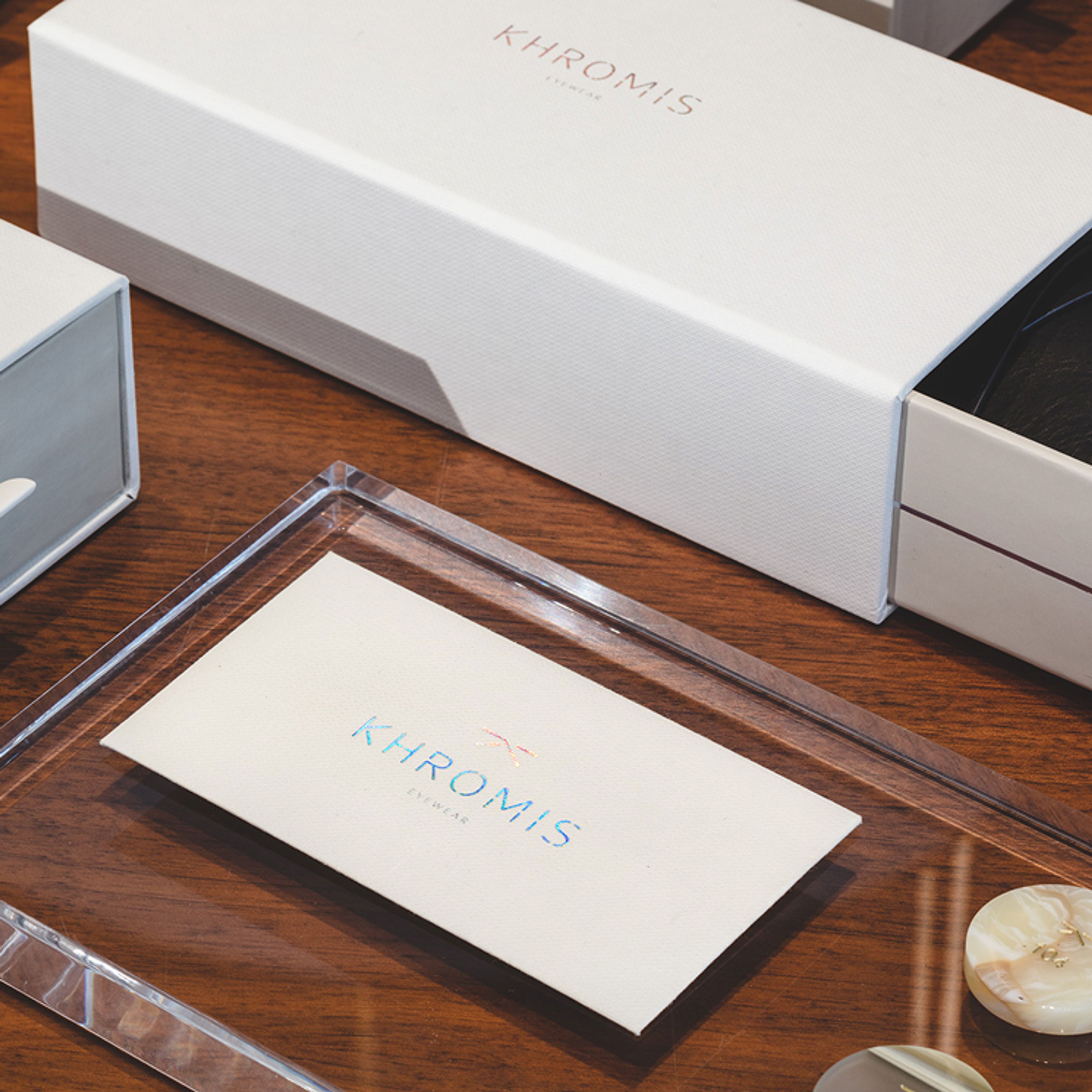 Partially open white box and a card, both with Khromis Eyewear branding, on a wooden table.