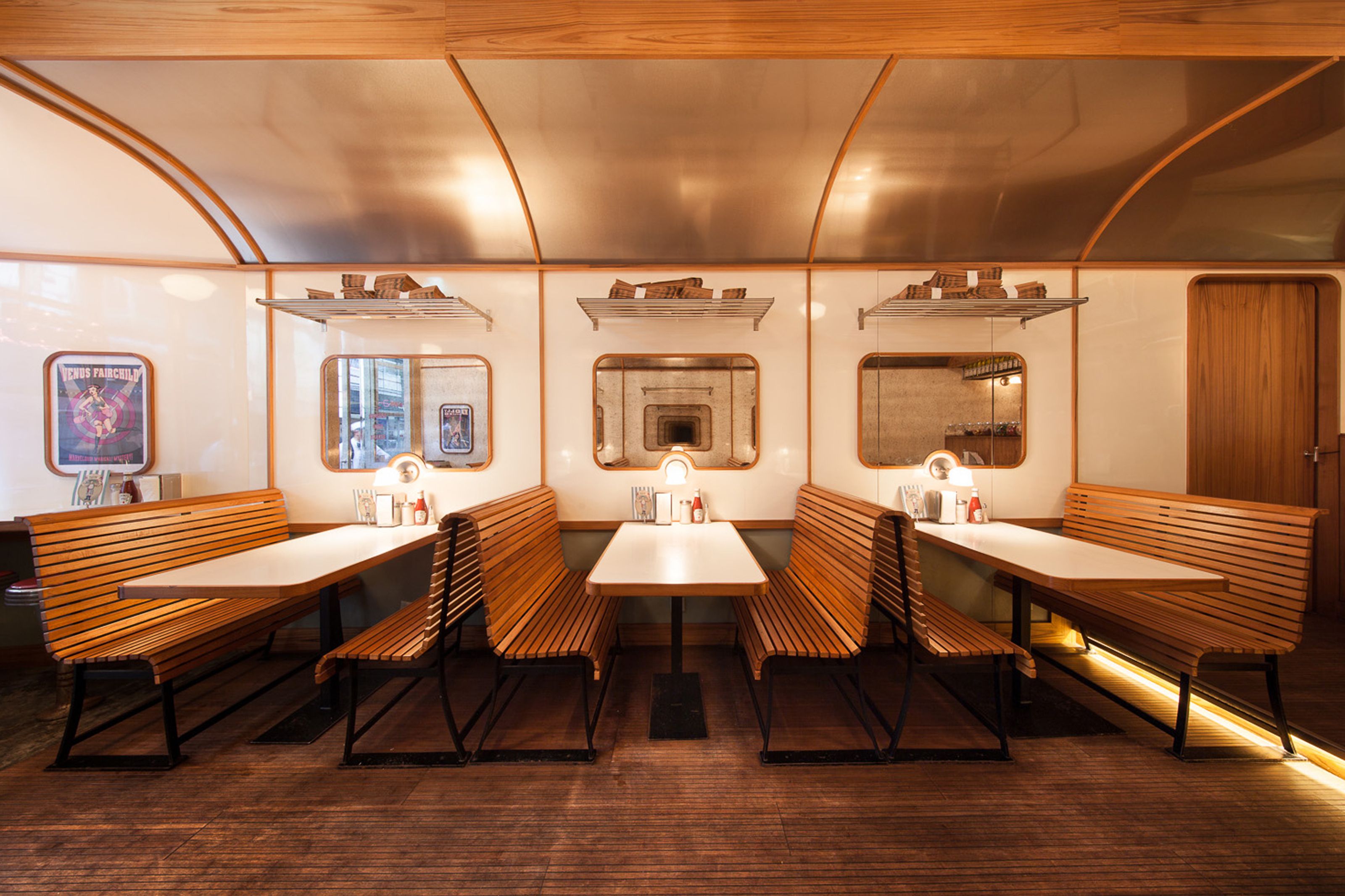Interior of a diner-style restaurant with slatted wooden booths, white tables, and walls designed to resemble a train carriage.