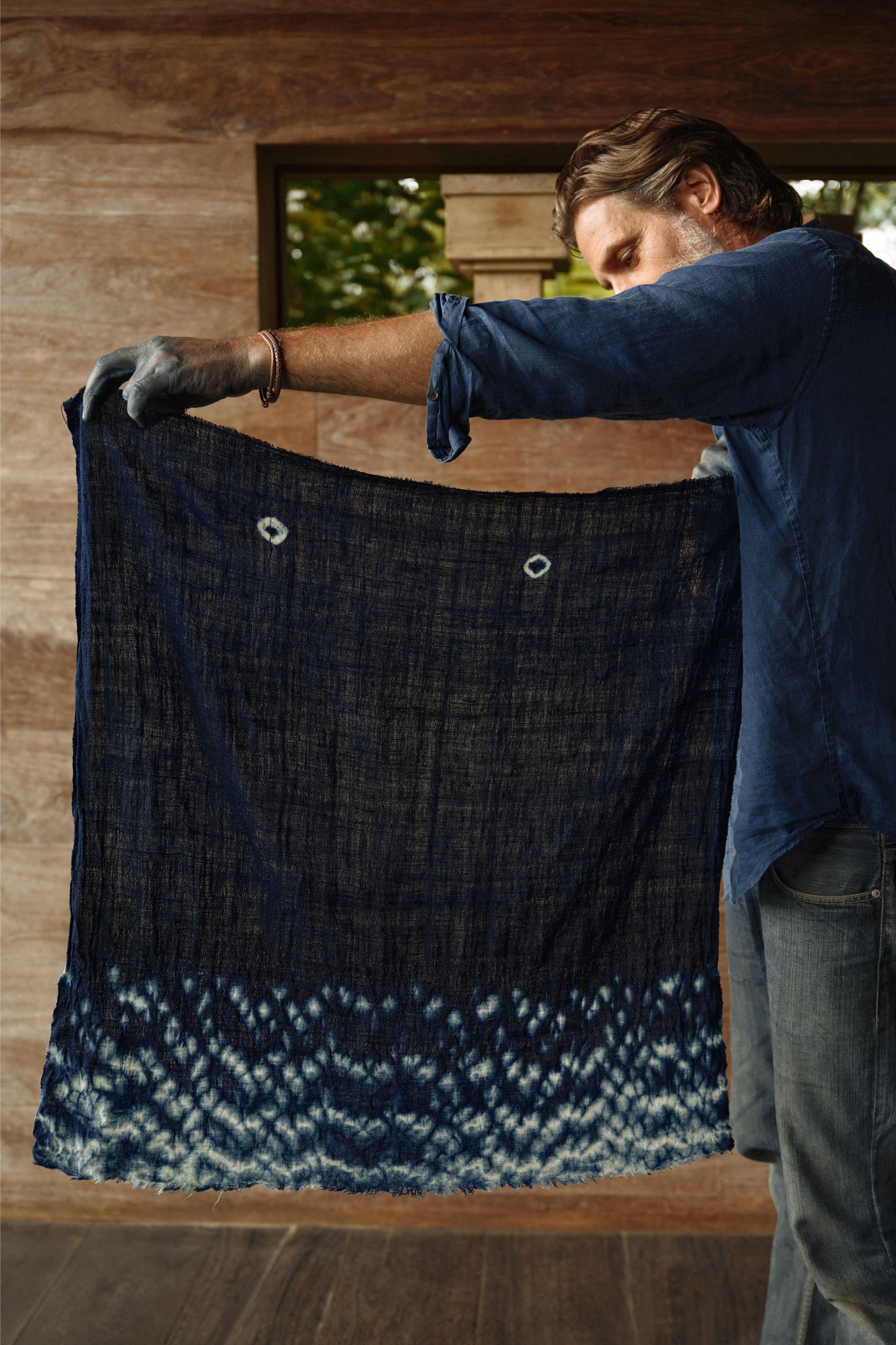 A man wearing gloves holds a dark blue shibori fabric with white patterns.