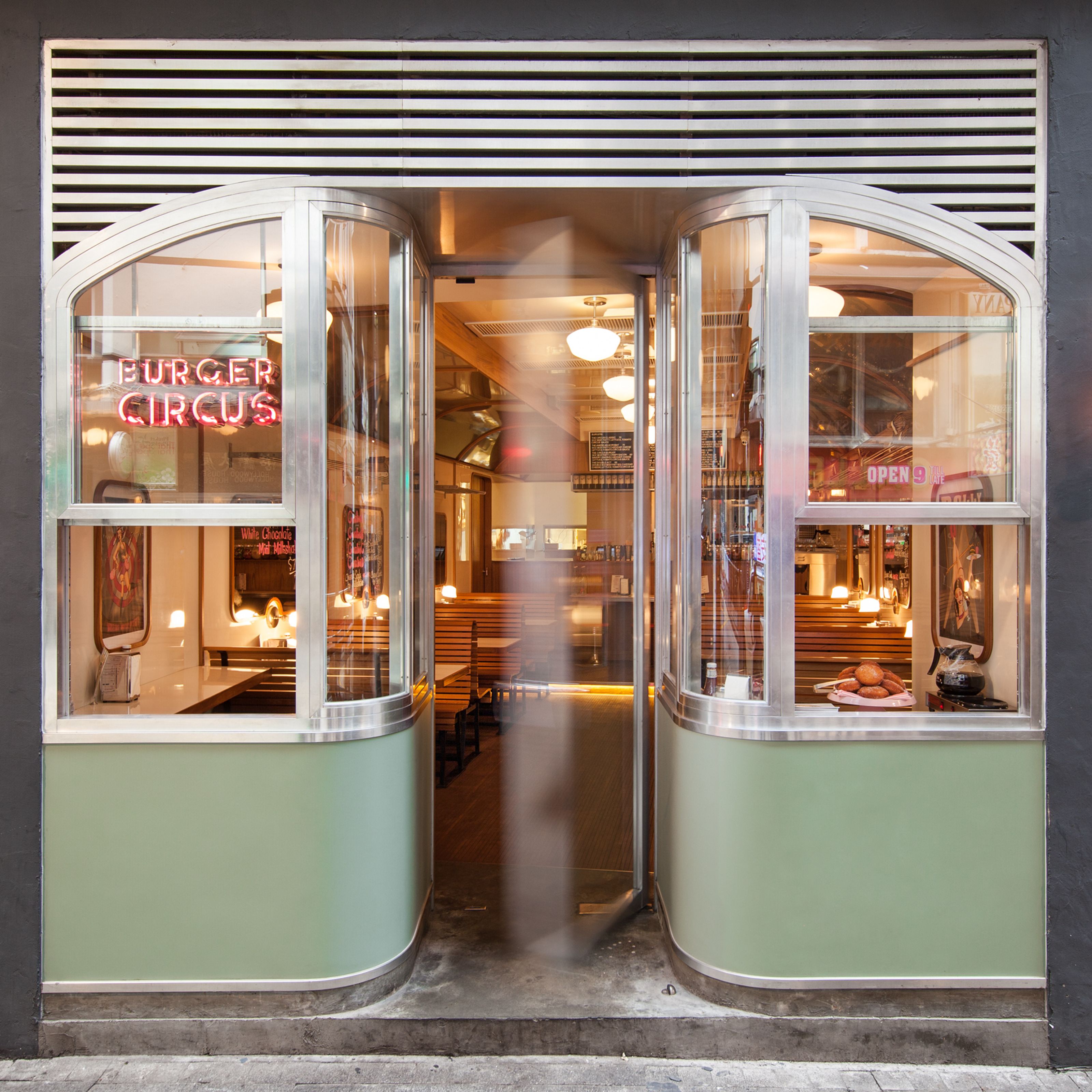 Retro diner entrance with a neon "Burger Circus" sign, curved windows, and light green panels.