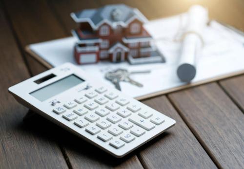 A calculator in front of a Villa house model with a blueprint