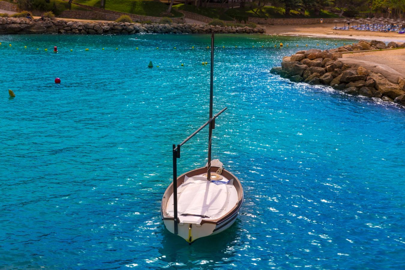 Lille båd ligger for anker i en rolig bugt med turkisblåt vand og sandstrand i baggrunden.
