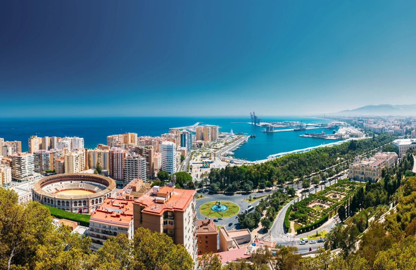 Billedet er over Malaga by og er taget fra udsigtspunktet Mirador de Gibralfaro. Til venstre i billedet ser vi tyrefægterarenaen Plaza de Toros 'La Malagueta' omgivet af høje boligblokke, der også er bygget ud mod havet. Ud mod højre i billedet ses en større trafikeret aveny i retning mod centrum, som er omgivet af masser af beplantning og parkanlæg. Længst inde i billedet ser vi havneområdet med noget industri, havet og en skyfri himmel.
