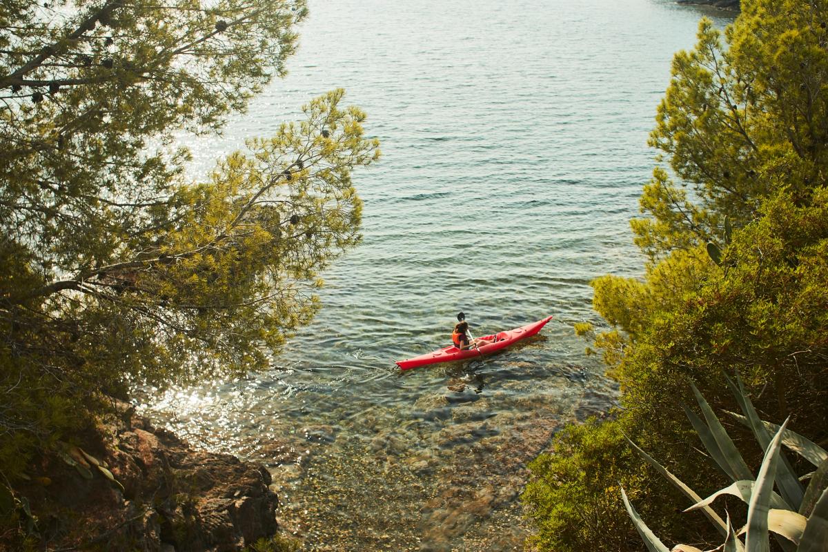 En kajak flyter stilla på det klara Medelhavet, med gröna träd och låga klippor som skymtar längs Costa Brava-kusten
