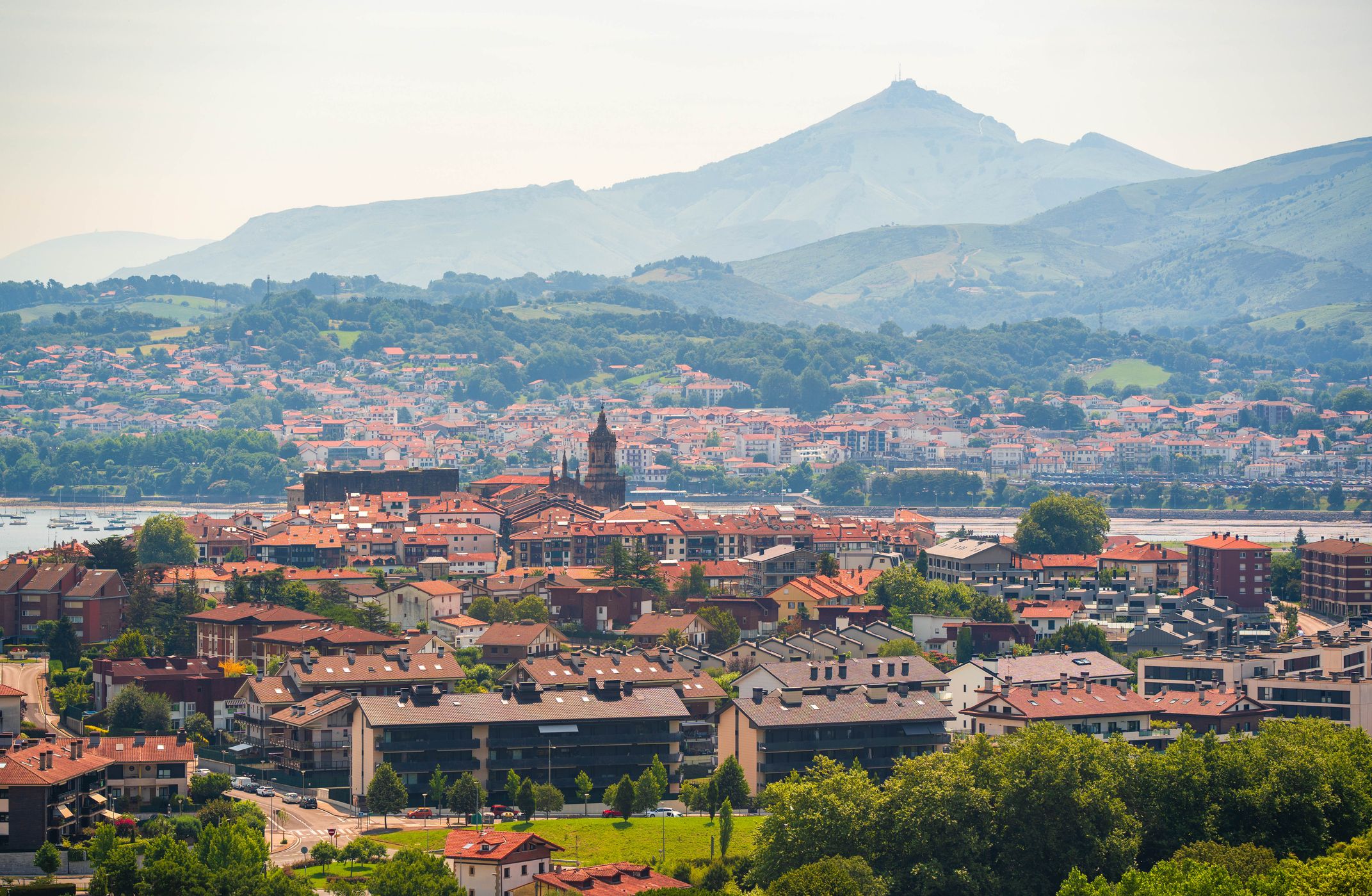 Utsikt over Hondarribia. I forgrunnen ligger flere hus med røde takstein, et kirketårn stikker opp, og i bakgrunnen reiser det grønne landskapet og fjellene seg.