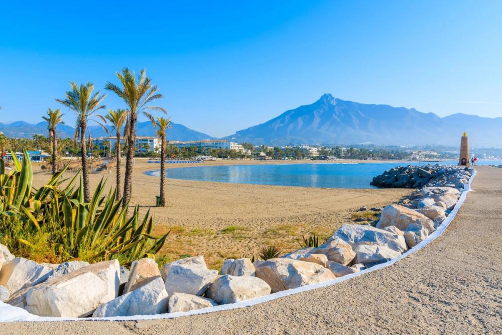 Strandpromenaden i Puerto Banus med utsikt over stranden og langgrunne sjøen, med spredde palmer