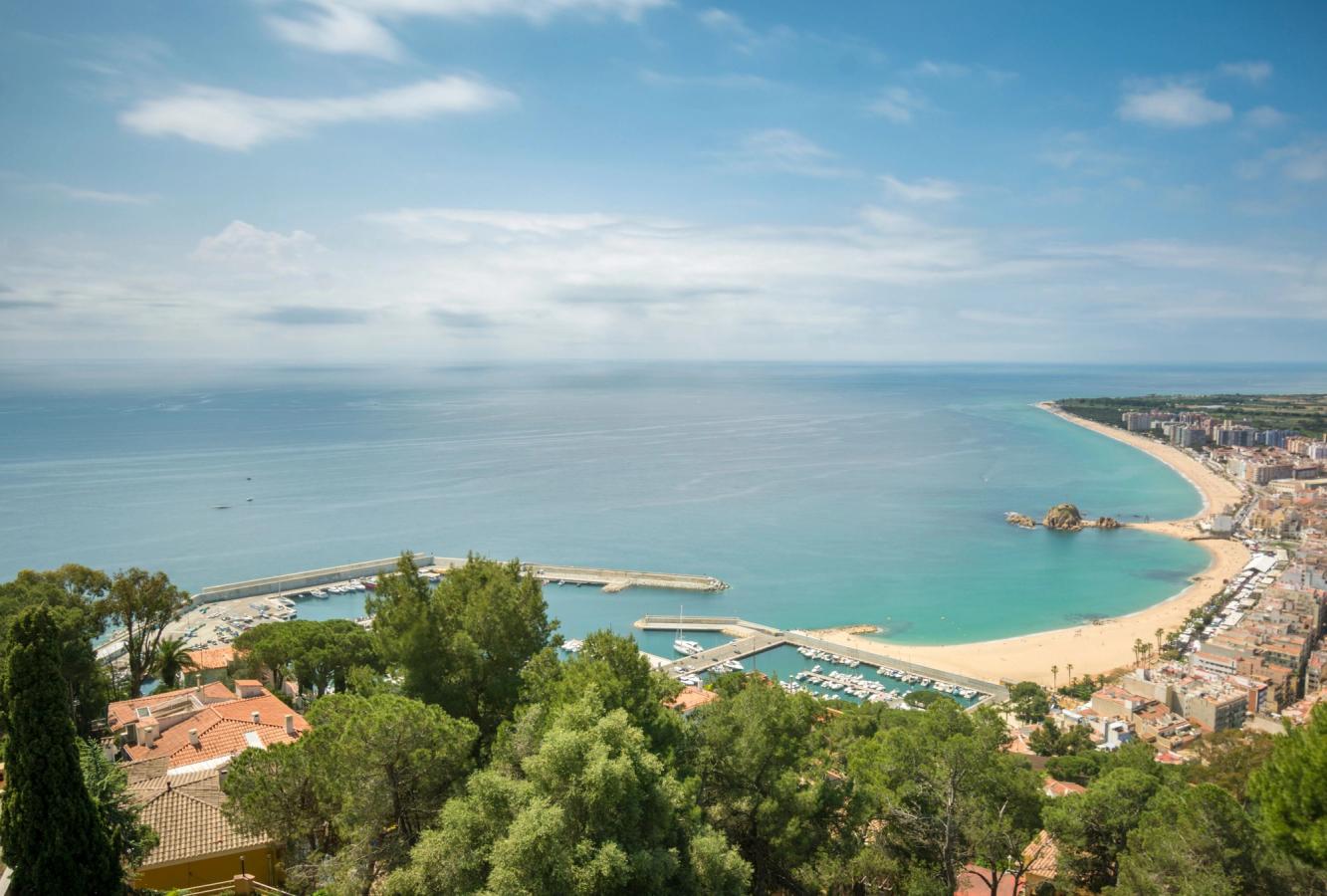 Billedet viser, set fra oven, hele den lange bystrand i Blanes. Her med et lille havneområde til venstre i billedet og Costa Bravas lange kyststrækning.
