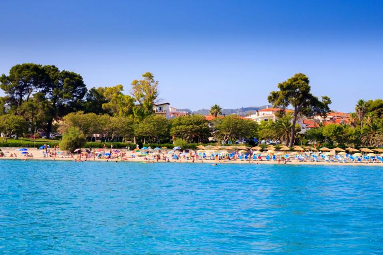 Utsikt över det turkosa vattnet och stranden med staden Hanioti i bakgrunden på Kassandras halvö i Halkidiki, Grekland