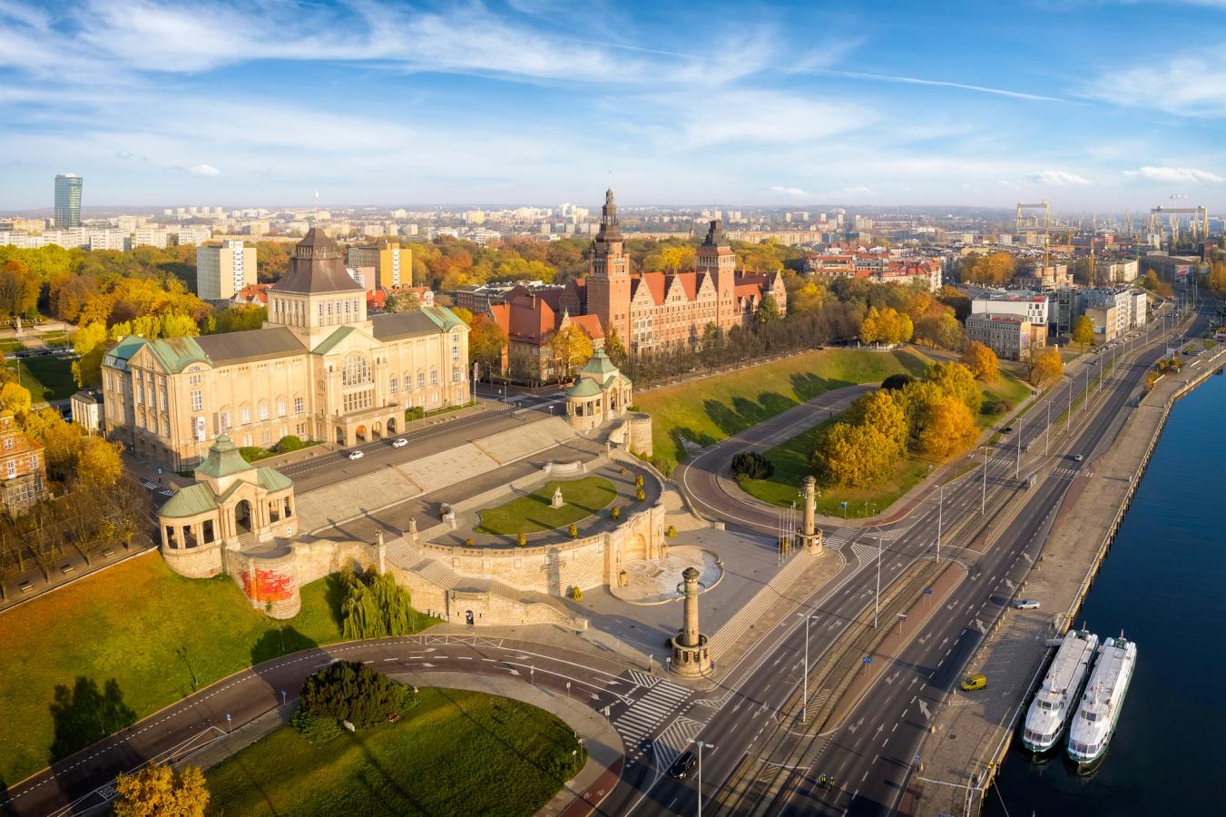 Billedet viser Haken Terrace og Wały Chrobrego, en af hovedattraktionerne i Szczecin. Til højre i billedet ses floden Oder med to sightseeingbåde, der ligger til kaj. Ind mod venstre løber en trafikåre, som går over i en vold og terrasse med to store, ældre bygninger, der udgør Szczecin Voivodeship Office.