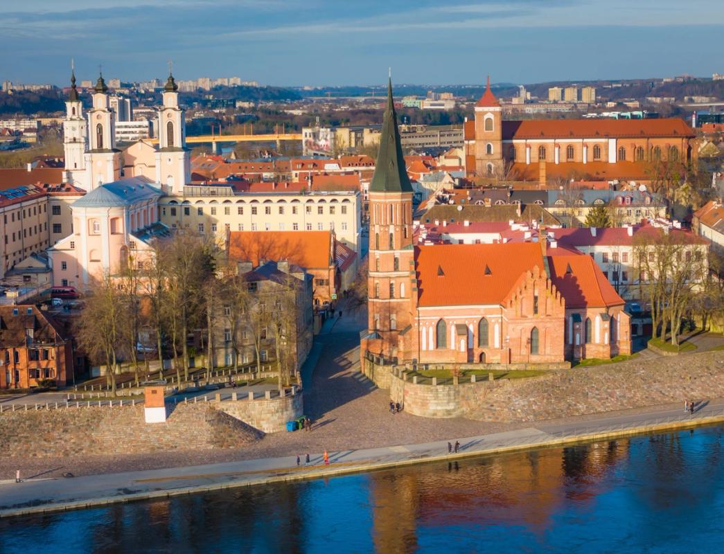 Kaunas gamla stad med historiska byggnader, däribland en röd tegelkyrka med torn, omgiven av floden Nemunas och en kullerstensbelagd promenad.