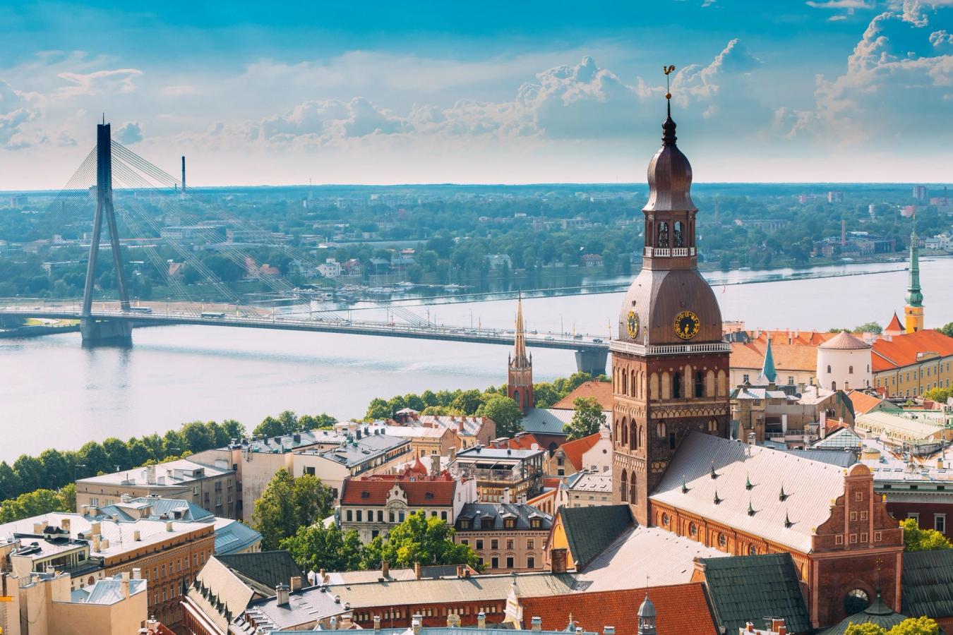 Riga By med gamle bygårder i forgrunnen og en flott bro som strekker seg over elven Daugava i bakgrunnen