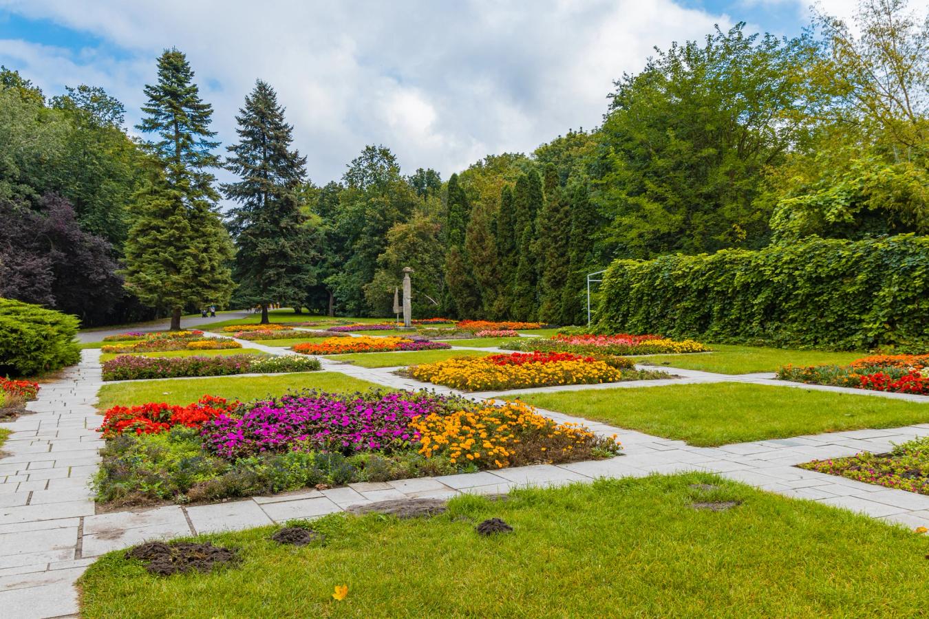 Bildet viser flere fargerike blomsterbed med gangveier mellom bedene i Park Cytadela i Poznan. Blomstene er omgitt av frodig og grønn beplantning.