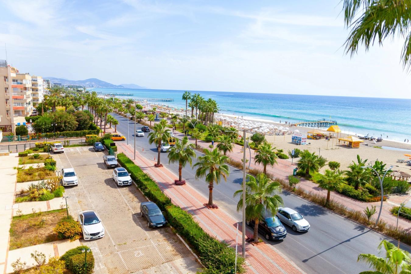 Utsikt over strandpromenaden og den langstrakte, deilige stranden med azurblått hav i Alanya på Antalyakysten i Tyrkia