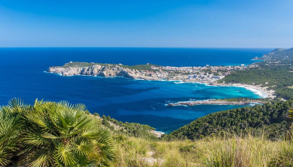 Bilde tatt fra høyden over Cala Ratjada, hvor du ser bukten foran byen med det blå krystallklare vannet. Bukten ender i en blanding av lange sandstrender og mer vegetasjon