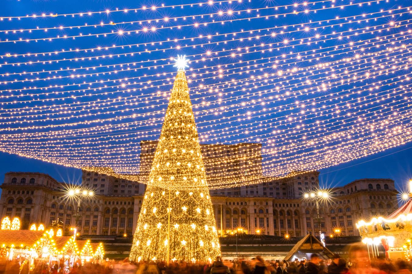Bildet viser julemarked i Bucuresti på kveldstid. Et opplyst juletre midt i bildet, med parlamentsbygningen i bakgrunnen.