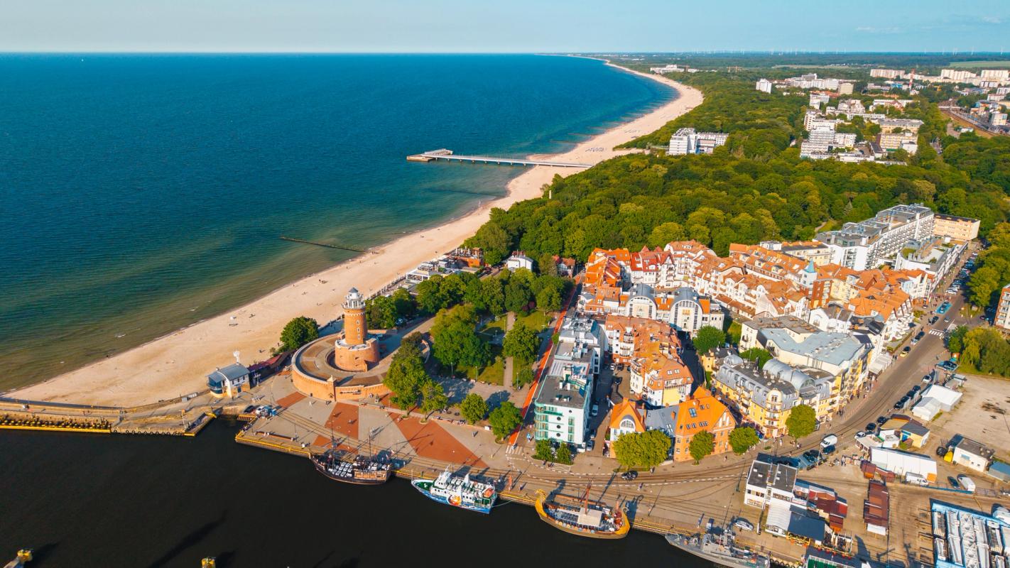 Bildet viser hjørnet mellom bystranden og strandpromenden hvor fyrtårnet er utgangspunktet for begge retninger. Stranden på venstre side i bildet, fyrtårnet i midten og promenaden med bebyggelse langs høyre side.