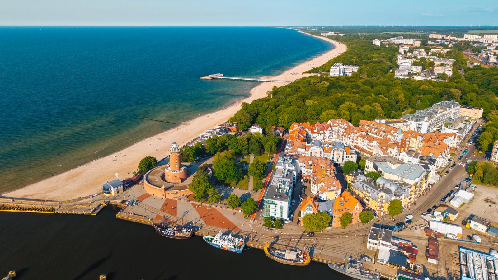 Billedet viser hjørnet mellem bystranden og strandpromenaden, hvor fyrtårnet markerer udgangspunktet for begge retninger. Stranden ses til venstre i billedet, fyrtårnet i midten og promenaden med bebyggelse langs højre side.