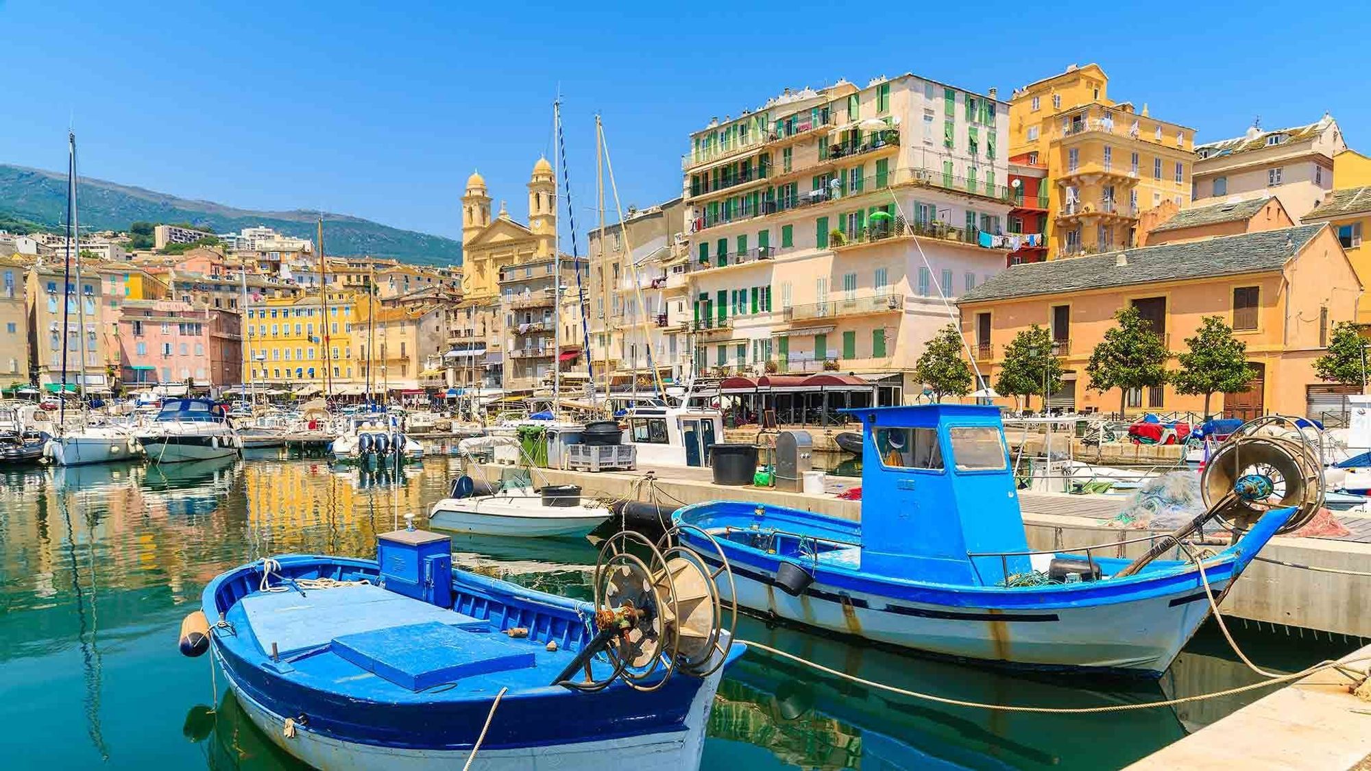 Havneområdet i Bastia på Korsika. Fremst i bildet med to mindre blå fiskeskøyter og med bebyggelse i bakgrunnen.