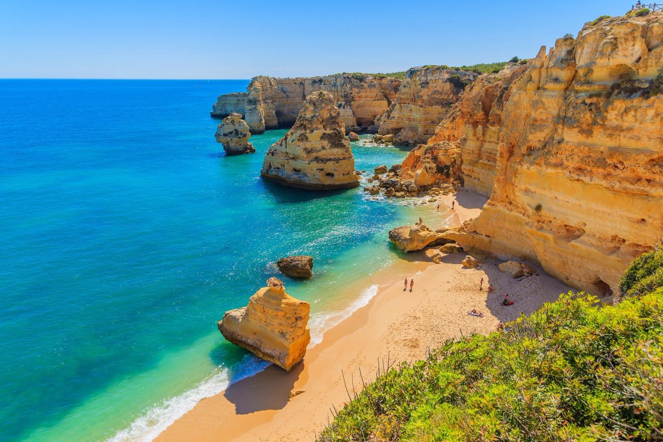 Vi ser den populära stranden "Praia da Marinha" från en höjd. Stranden slutar tvärt i branta klippväggar i sandfärg. Vattnet har en blåturkos färg.