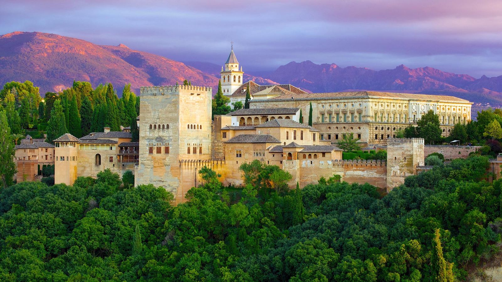 Palasset Alhambra ved Granada I Andalucia sees i forkant av fjellformasjon, omgitt av frodig natur
