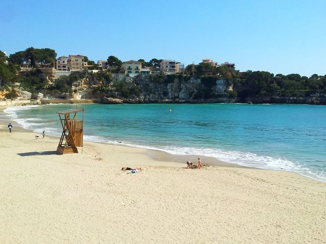 Bildet viser bukta inn mot stranden i Porto Cristo, omfavnet av klippevegg og bebyggelse. Stranden er langgrunn og finkornet, som ellers på Mallorca