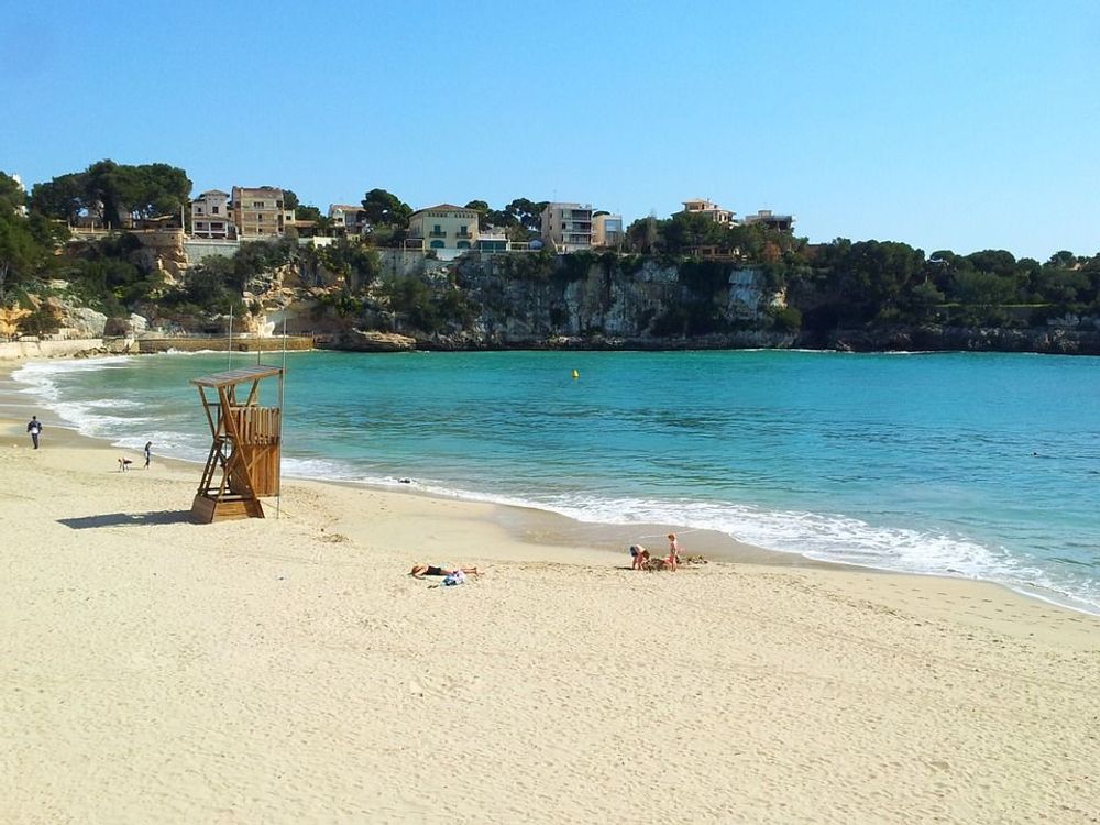 Bildet viser bukta inn mot stranden i Porto Cristo, omfavnet av klippevegg og bebyggelse. Stranden er langgrunn og finkornet, som ellers på Mallorca