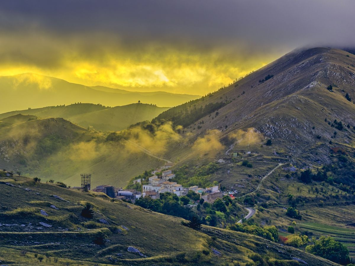 Stämningsfull bild över staden Santo Stefano di Sessanio i området Abruzzo i Italien. Staden ligger i en frodig dalgång där ett lätt molntäcke vilar över hustaken medan solljuset tränger igenom.