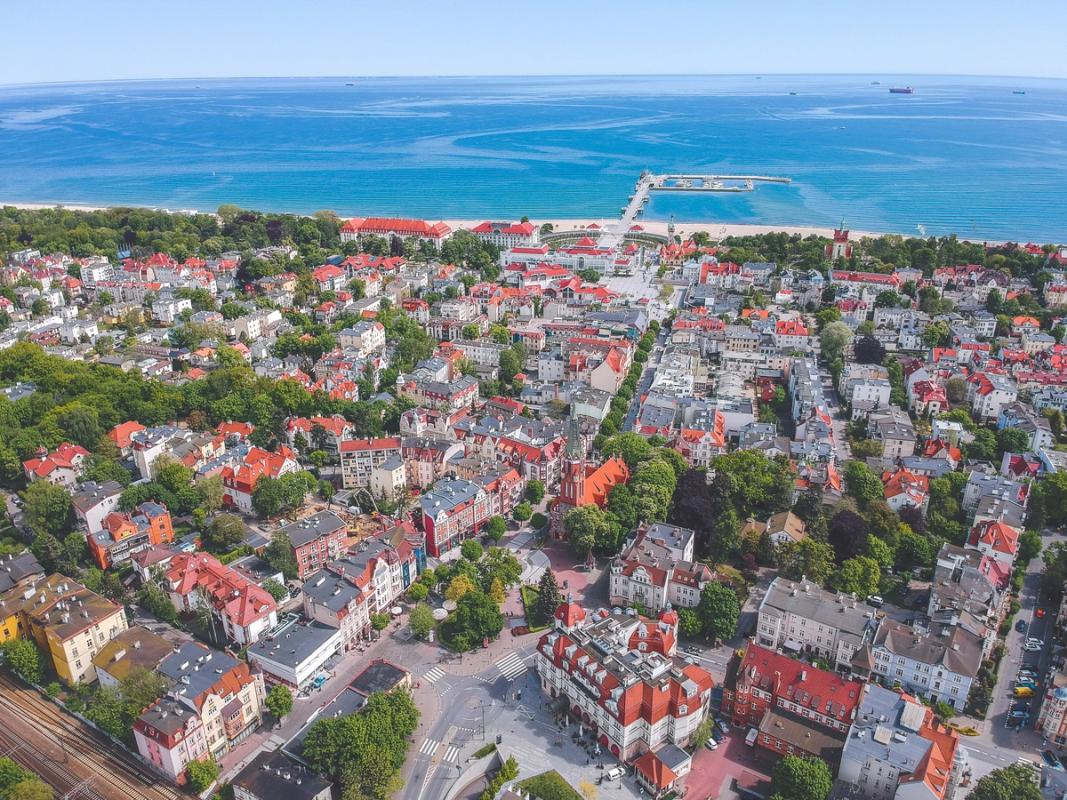 Bildet viser et oversiktsbilde av Sopot by. Her vises byens bygningsmasse med klassiske røde tak og spredt grønn beplantning i gatene. Byen ender ut i sandstranden langs den blåe Østersjøen.