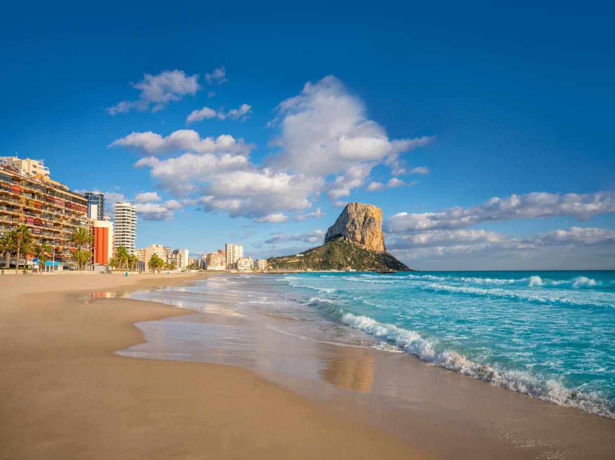 Renal-Bol Beach i Calpe med gyllen sand, klart blått vann og klipper i bakgrunnen.