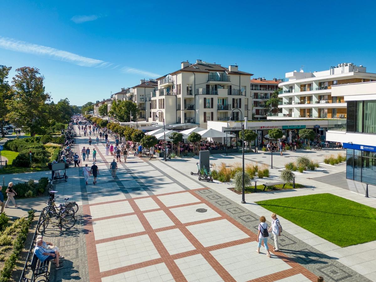 Bilden visar strandpromenaden i Swinoujscie. I mitten av bilden ser vi gågatan som är belagd med stenplattor och människor som flanerar. Till höger ser vi olika byggnader med trottoarcaféer och lägenheter ovanför.