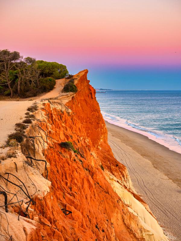 Solnedgang over Praia da Falésia med røde klipper til venstre og sandstrand langs kysten