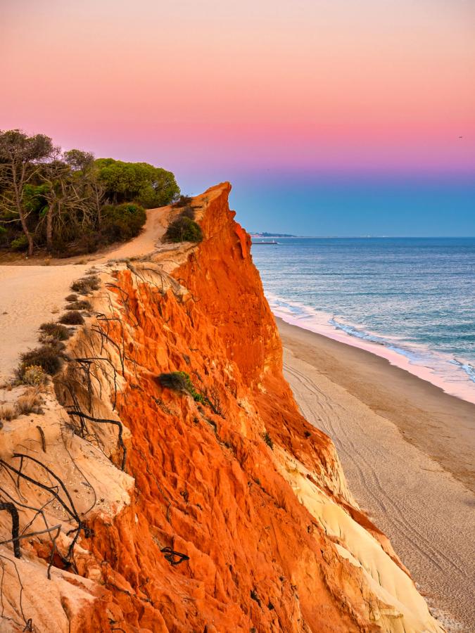 Solnedgang over Praia da Falésia med røde klipper til venstre og sandstrand langs kysten 