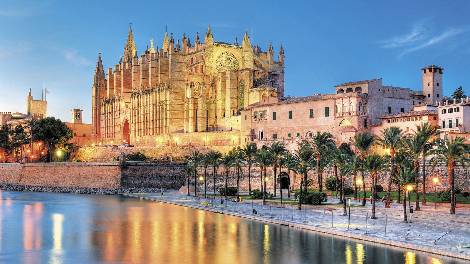 Bilden visar katedralen i Palma de Mallorca på kvällen, upplyst med större lampor. Stadsstranden ligger tyst och lugn framför katedralen
