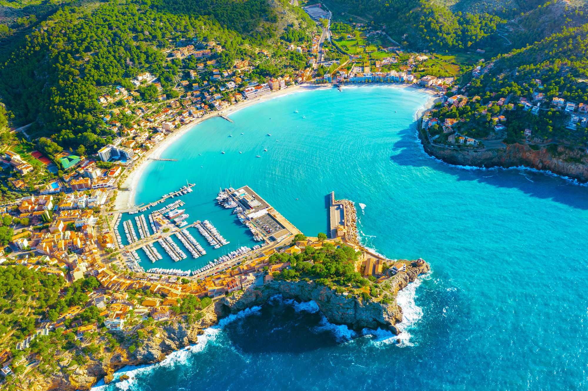 Udsigt over bugten og havnen i Port de Sóller på Mallorca i Spanien med frodig vegetation i baggrunden.