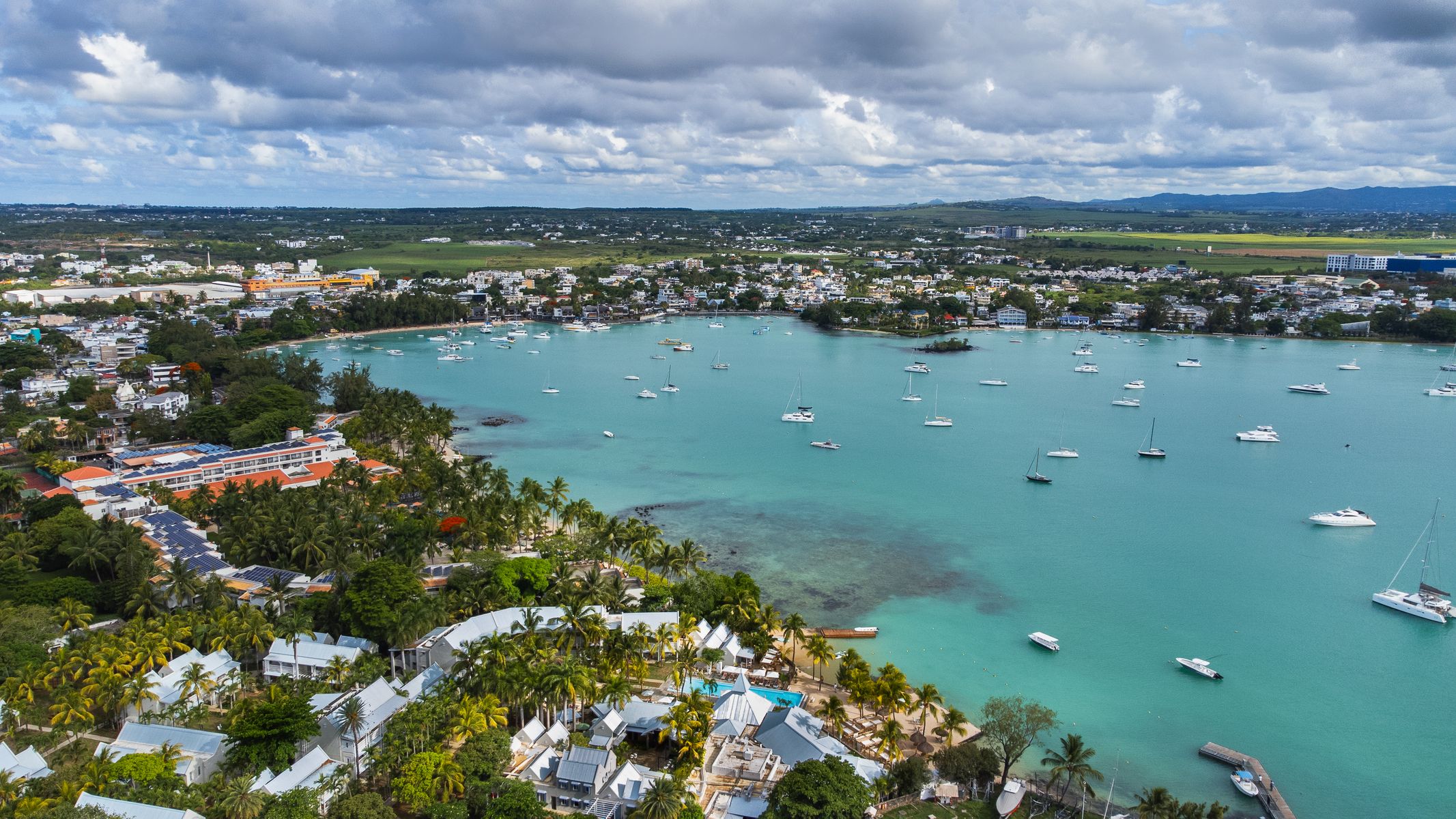 Grand Baie på Mauritius med turkisblått vann, lystbåter i lagunen og byen i bakgrunnen under en lett overskyet himmel.