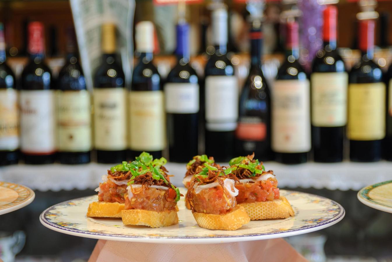 Bildet viser en tallerken med Pinxo (tapas) som opprinnelig kommer fra San Sebastian, med en rekke med vinflasker i bakgrunnen