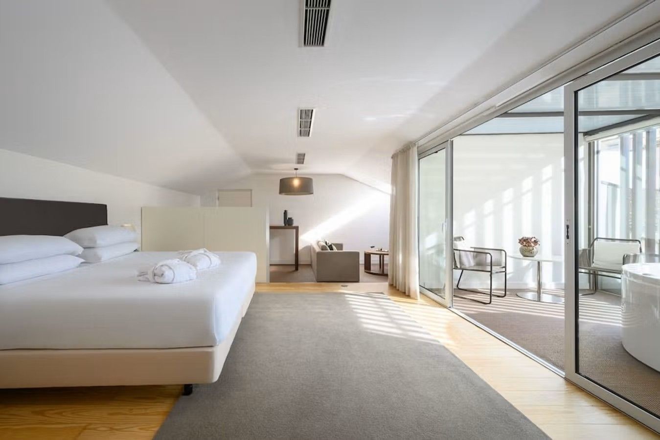 Från insidan av ett rum på hotellet Inspira Santa Marta i Lissabon i Portugal. Med stora, breda fönster som släpper in solljus över en bred, vit dubbelsäng och ljusa möbler.