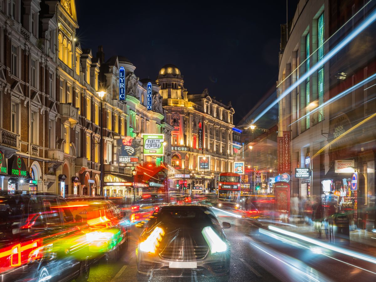 Bilden visar kvällstrafik på Shaftesbury Avenue, gatan i mitten av West End är upplyst av gatlyktor, reklam, men också från olika teatrar som visar aktuella föreställningar. Byggnaderna till vänster är av äldre arkitektur, som är upplysta med en mängd restauranger, butiker och teatrar
