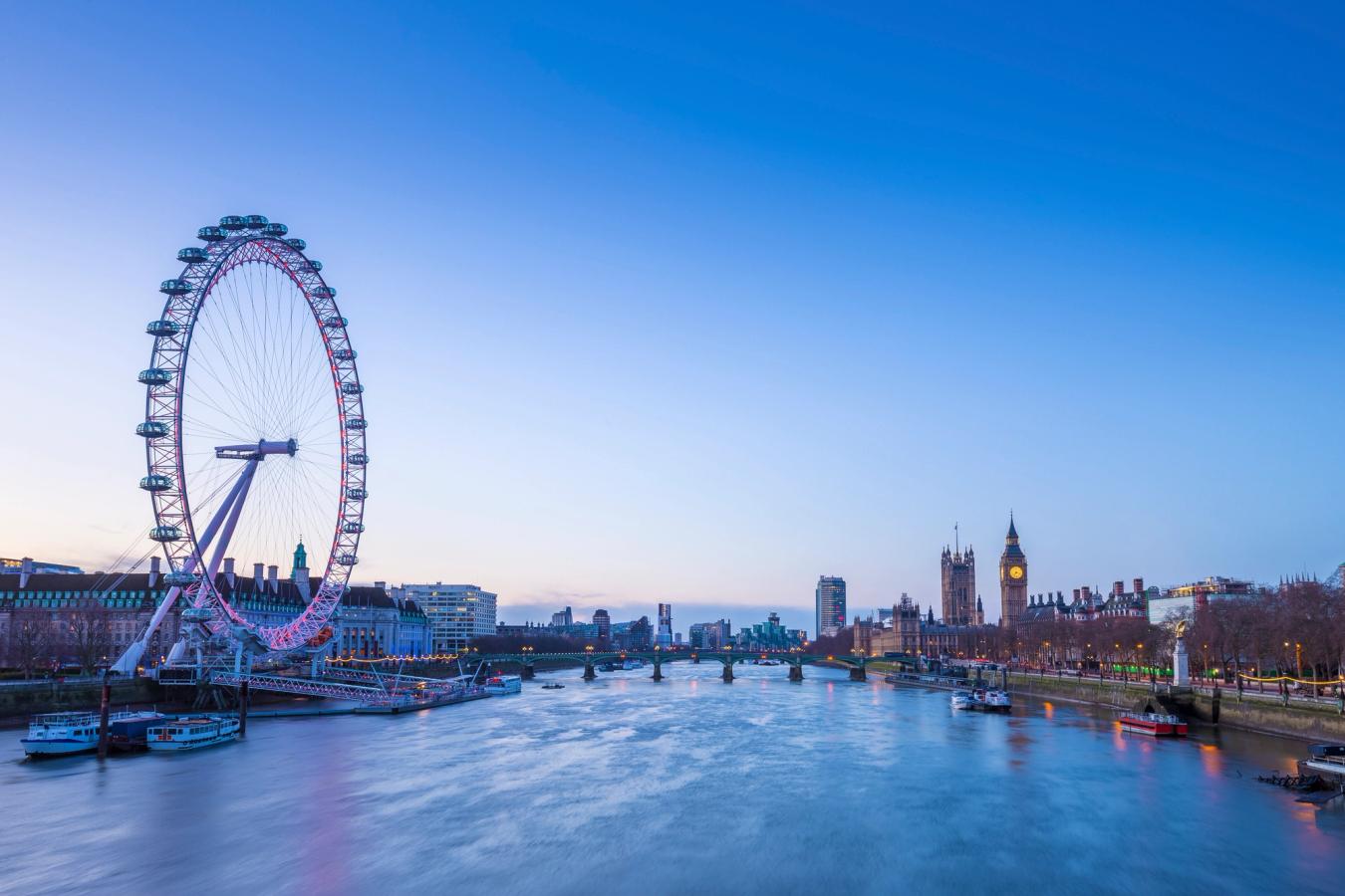 Bilden visar floden Themsen i blått skymningsljus. På vänster sida av floden ligger pariserhjulet London Eye. På flodens högra sida ser man några byggnader som slutar i klocktornet Big Ben och tornet på Westminster Hall. På andra sidan floden, framför Big Ben, ligger Westminster Bridge