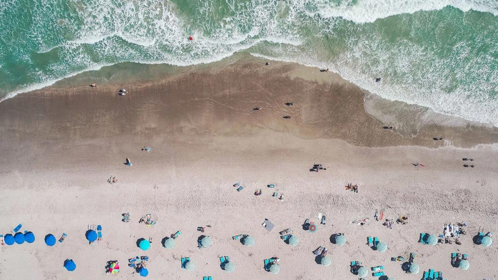 Parasoller och solstolar står på den gyllene sandstranden vid kusten, medan det blå havet glittrar i solen och vågorna rullar lugnt in mot land