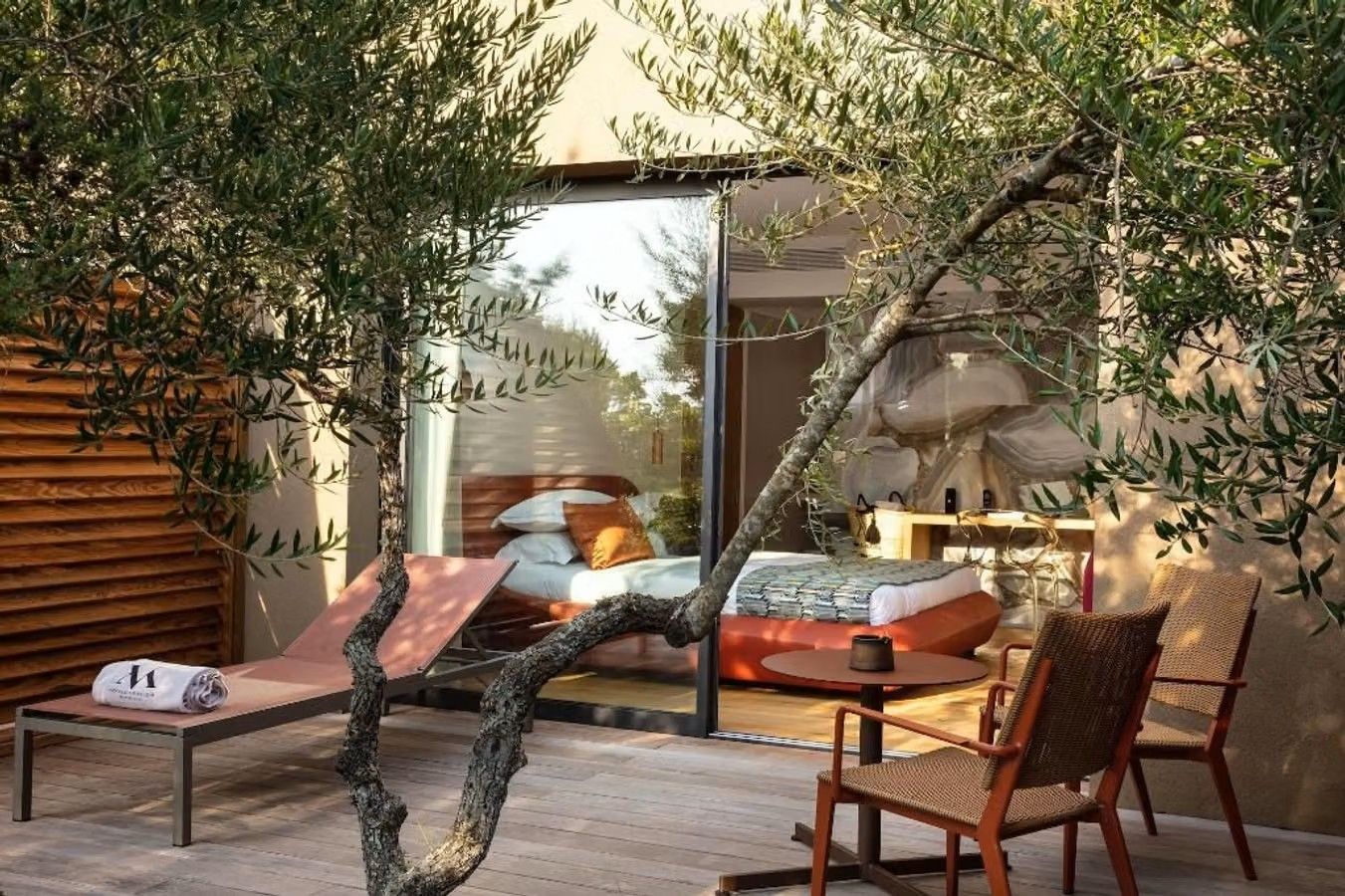 Et soverom på Hôtel et SPA Version Maquis Citadelle med sine store glassdører vender rett ut i egen terrasse med solseng og et oliventre som skygger for sola