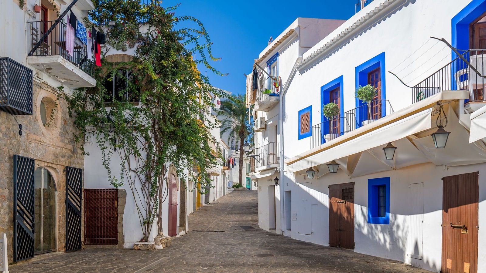 Bilden visar en mysig smal gata i Ibiza stad med kullerstensväg och vita hus