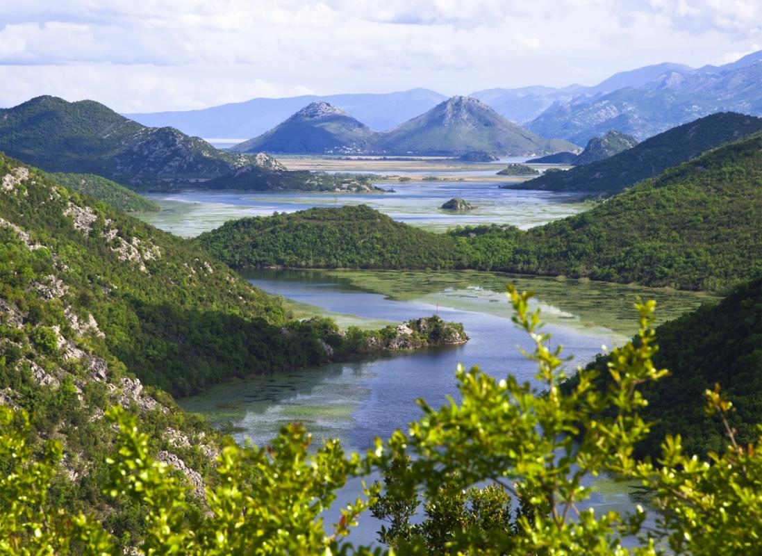 En stor innsjø som slynger seg inn og ut mellom flere fjell. Fjellene er frodige, og det er mye grønn vegetasjon. I bakgrunnen sees flere fjell.