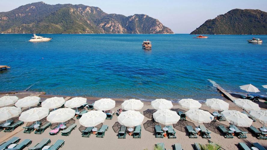 Stranden i Marmaris med båter ute på det krystallklare havet og fjell i bakgrunnen, Tyrkia