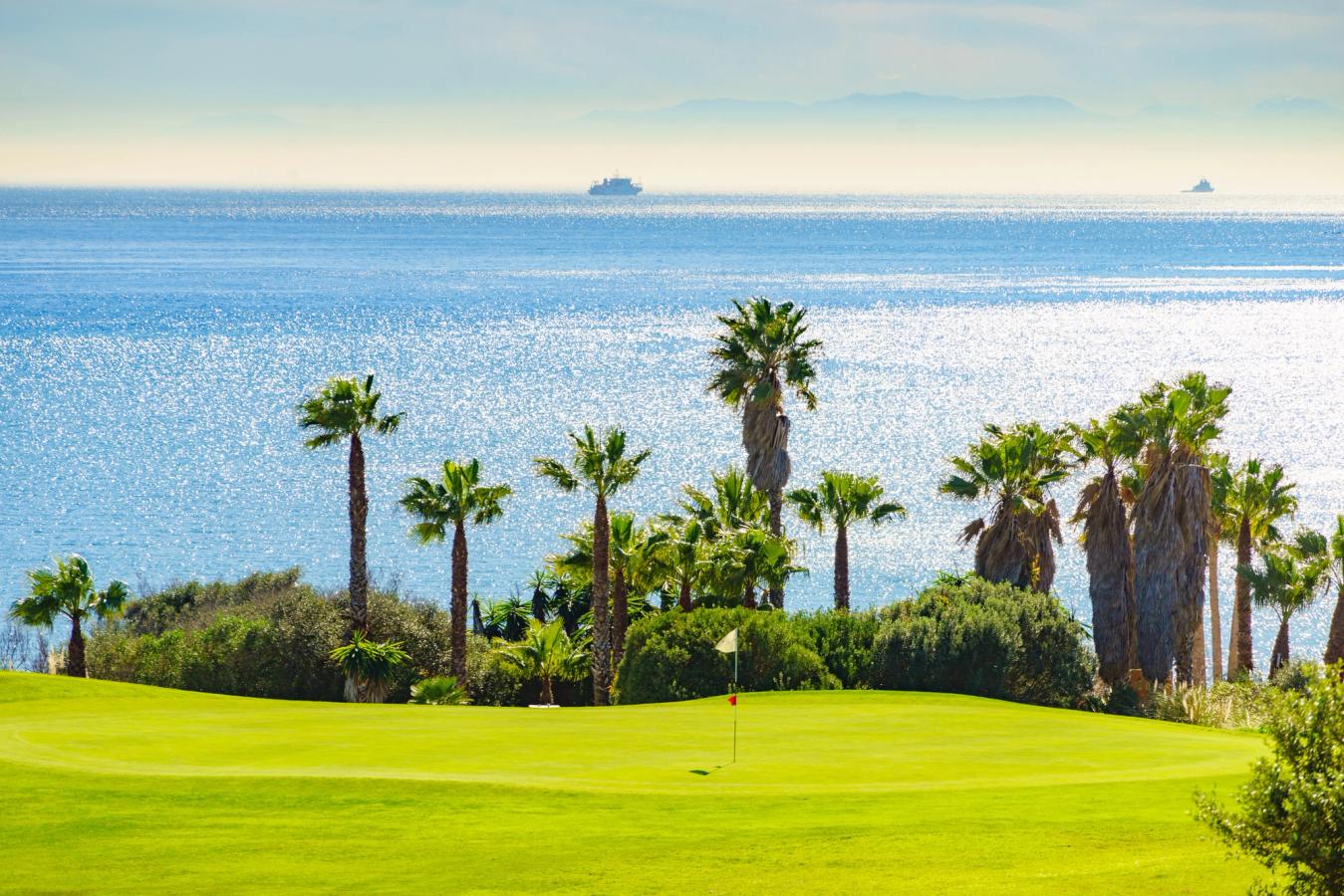 Sotogrande är känt för sin golf, och bilden visar en golfbana med palmer och havet i bakgrunden.