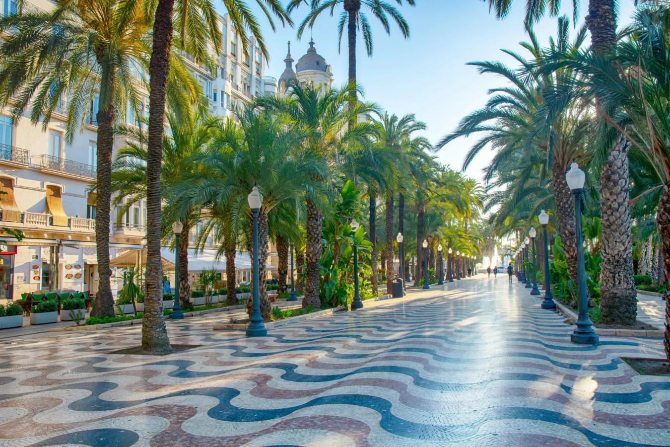 Billedet viser Alicantes store hovedpromenade, Explanada de España, som består af over 6 millioner røde, sorte og cremefarvede fliser, omkranset af palmetræer langs hele promenaden.