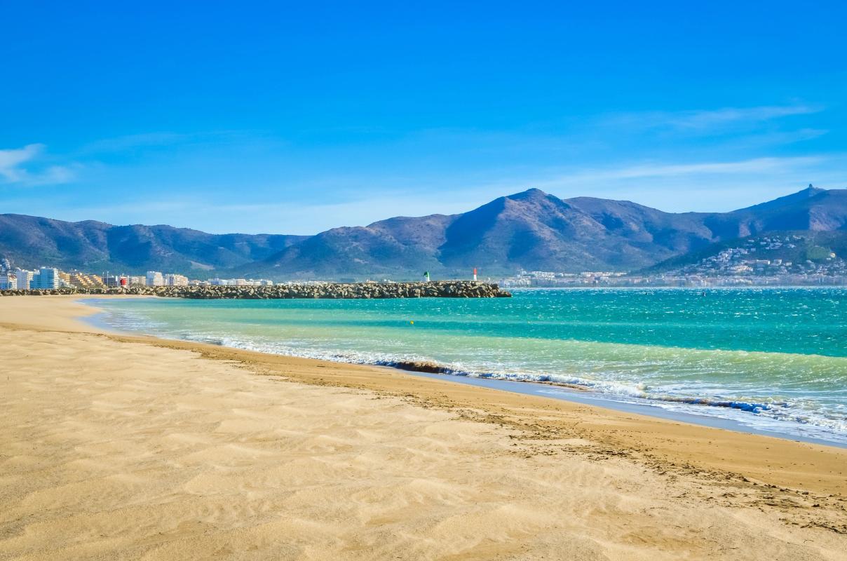 Bred sandstrand i Empuriabrava med gyllene sand och lugnt, klart medelhavsvatten under blå himmel